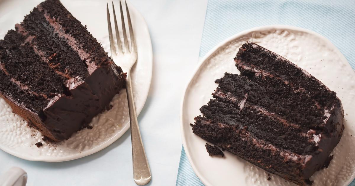 Two white plates with dark chocolate cake on them and a fork on the left plate.