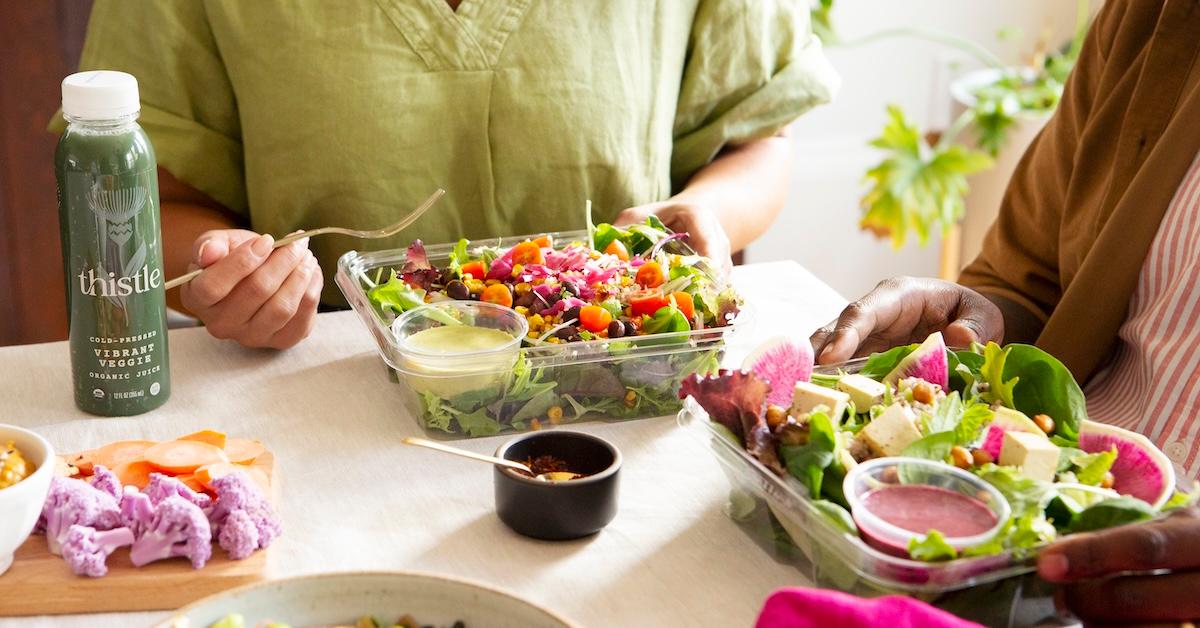 Two people sit at a table eating Thistle salads with a Thistle juice